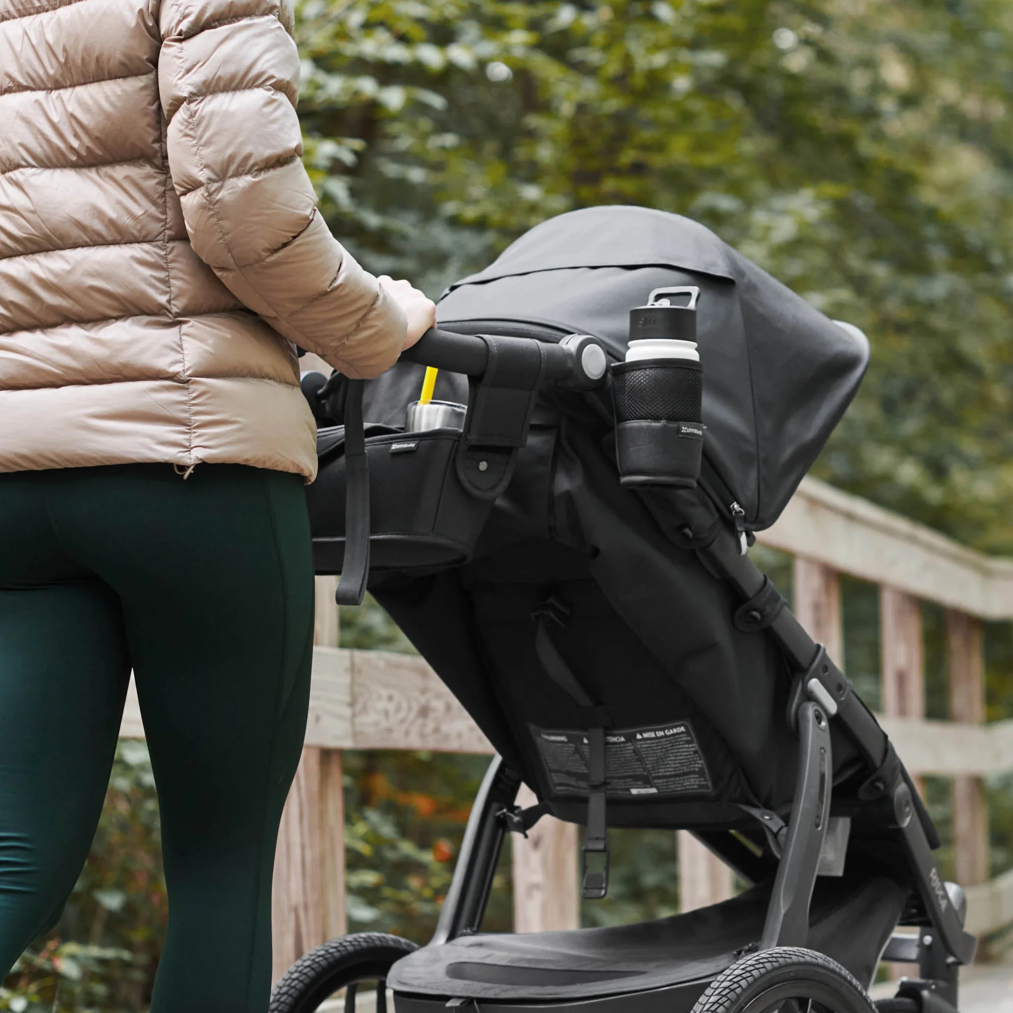 Parent walking with stroller outdoors featuring collapsible buggy cup holder for drinks, coffee cups and baby travel essentials on family walks