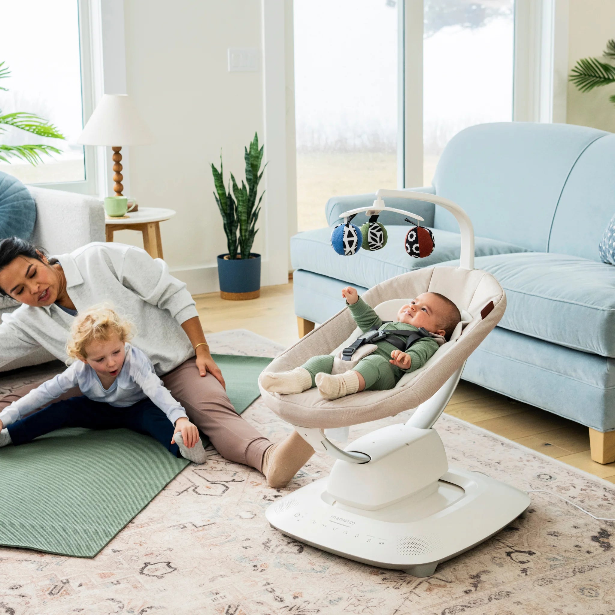 Mom and child doing yoga next to baby in Mamroo on living room floor.