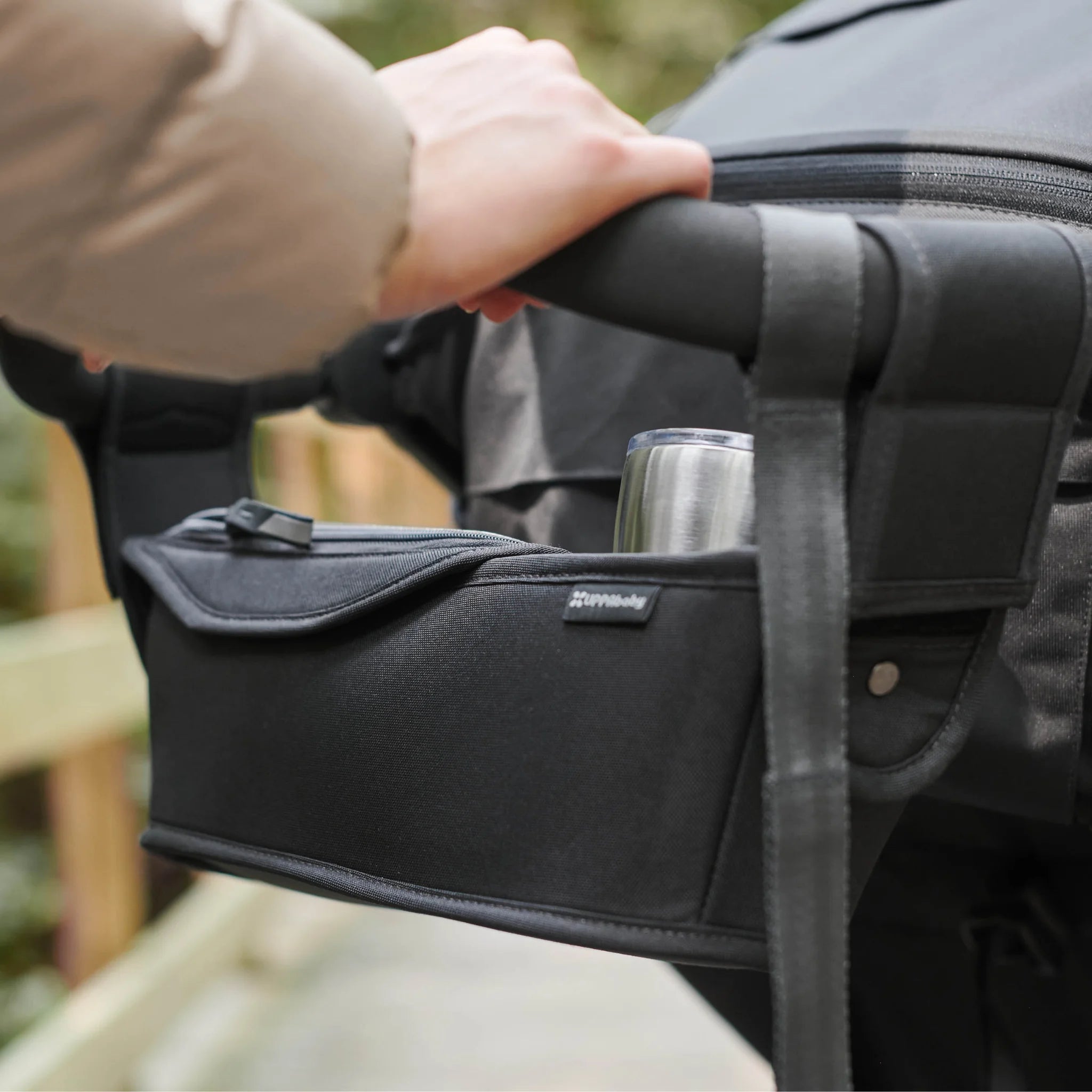 Lifestyle close-up of the UPPAbaby Ridge parent console attached to the stroller handlebar, showing the storage pocket and cup holder in use.