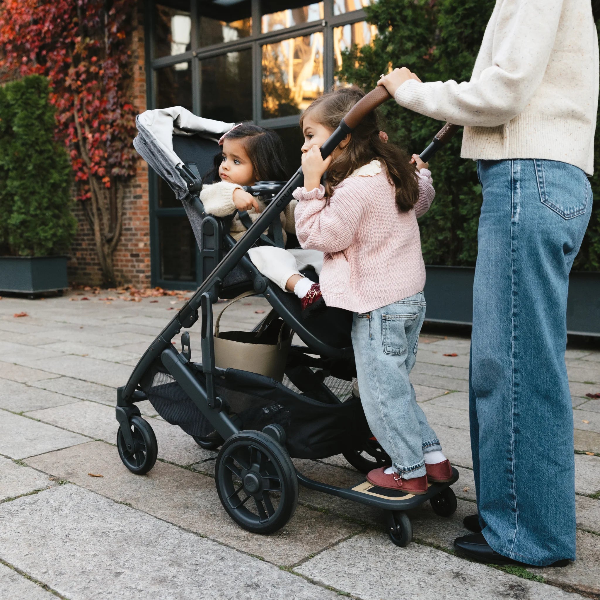 Kids looking into the distance from the cruz stroller. one is sitting in the buggy, while the other is standing on the cruz piggyback board,outside.