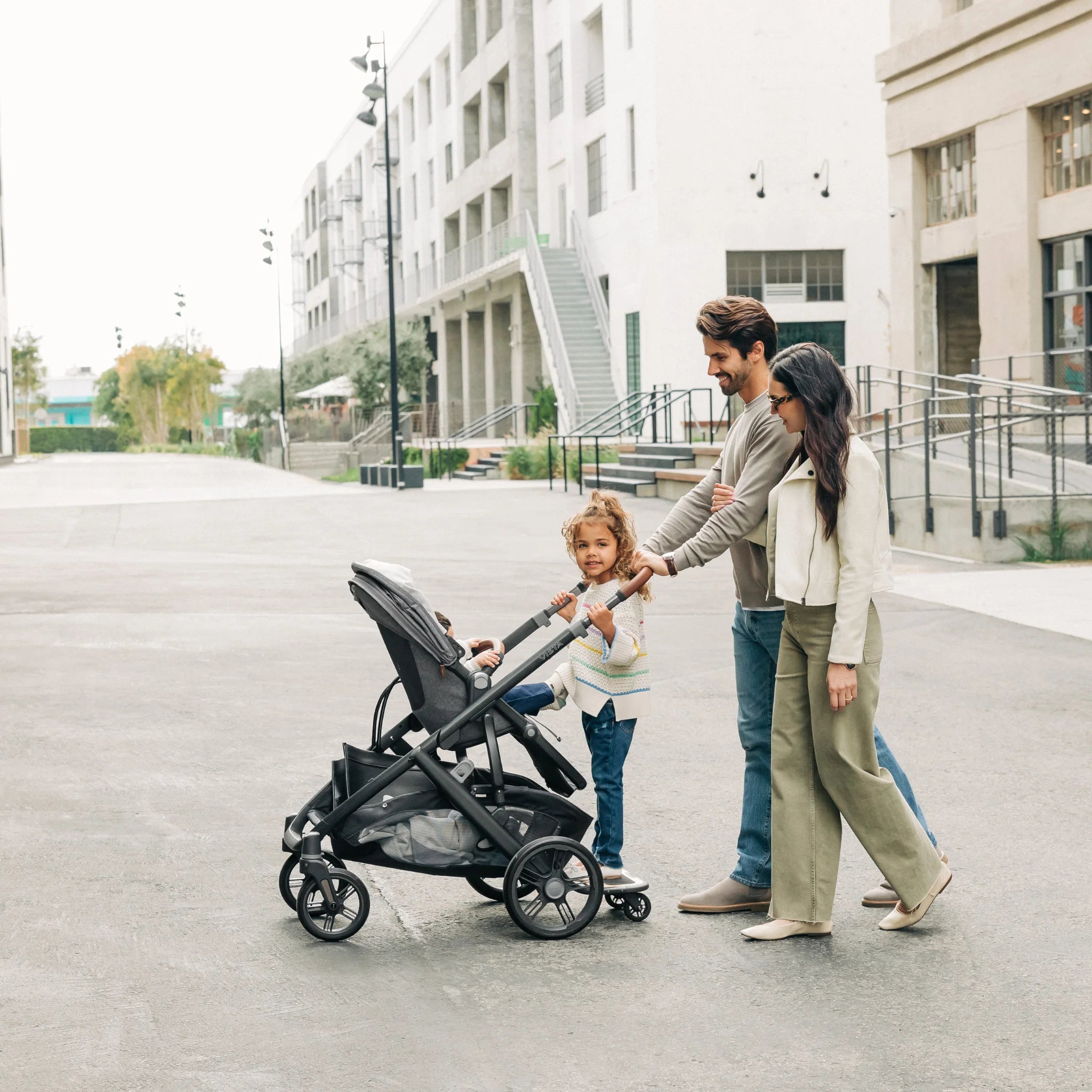 Family smiling, parents pushing vista buggy with vista piggyback board, outside.