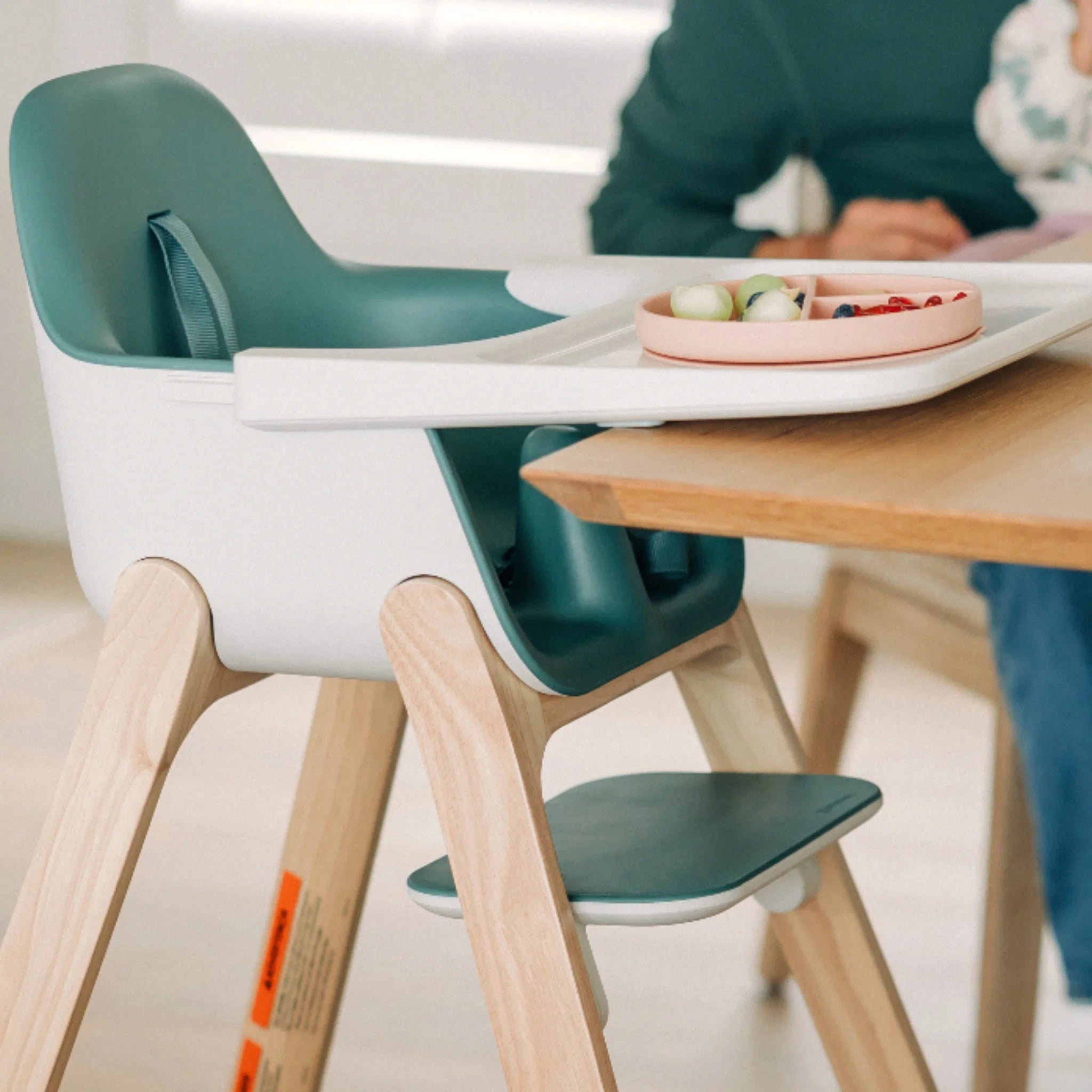Ciro high chair in Emrick pulled up to a wooden table, with a child’s plate of food on the tray.