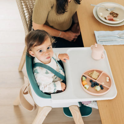 Toddler seated in the Emrick Ciro high chair at a dining table, with a snack plate and cup on the tray.