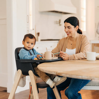 Toddler sitting in the Jake Ciro high chair beside a woman at a dining table in a bright kitchen.