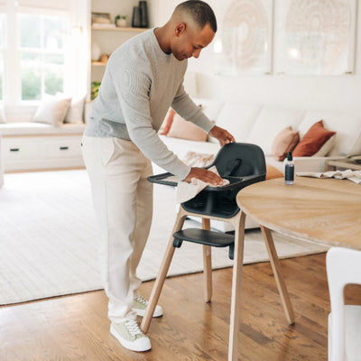 Adult wiping down the Jake Ciro high chair beside a dining table in a bright modern living space
