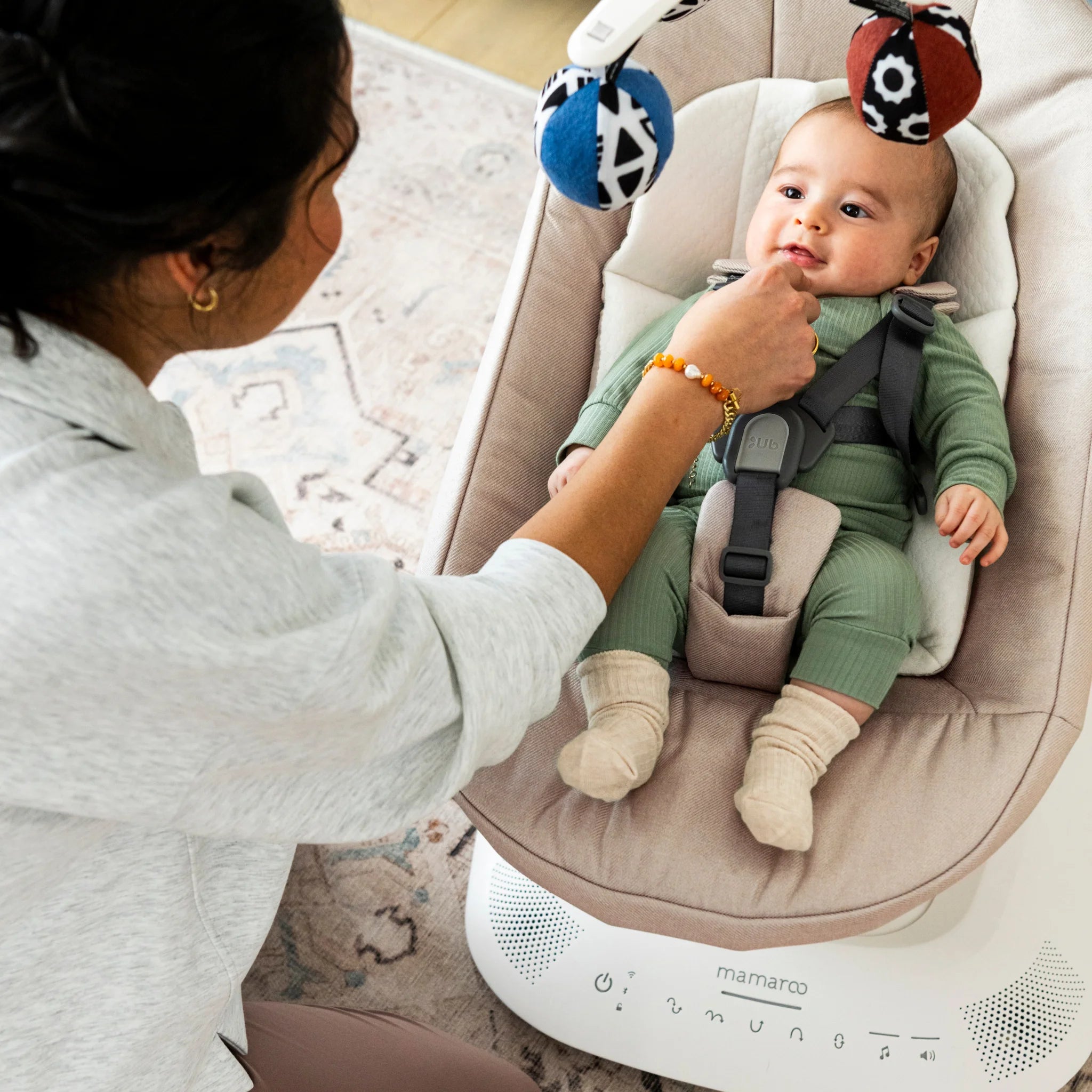 Baby in Mamaroo swing with mum smiling and touching mouth.