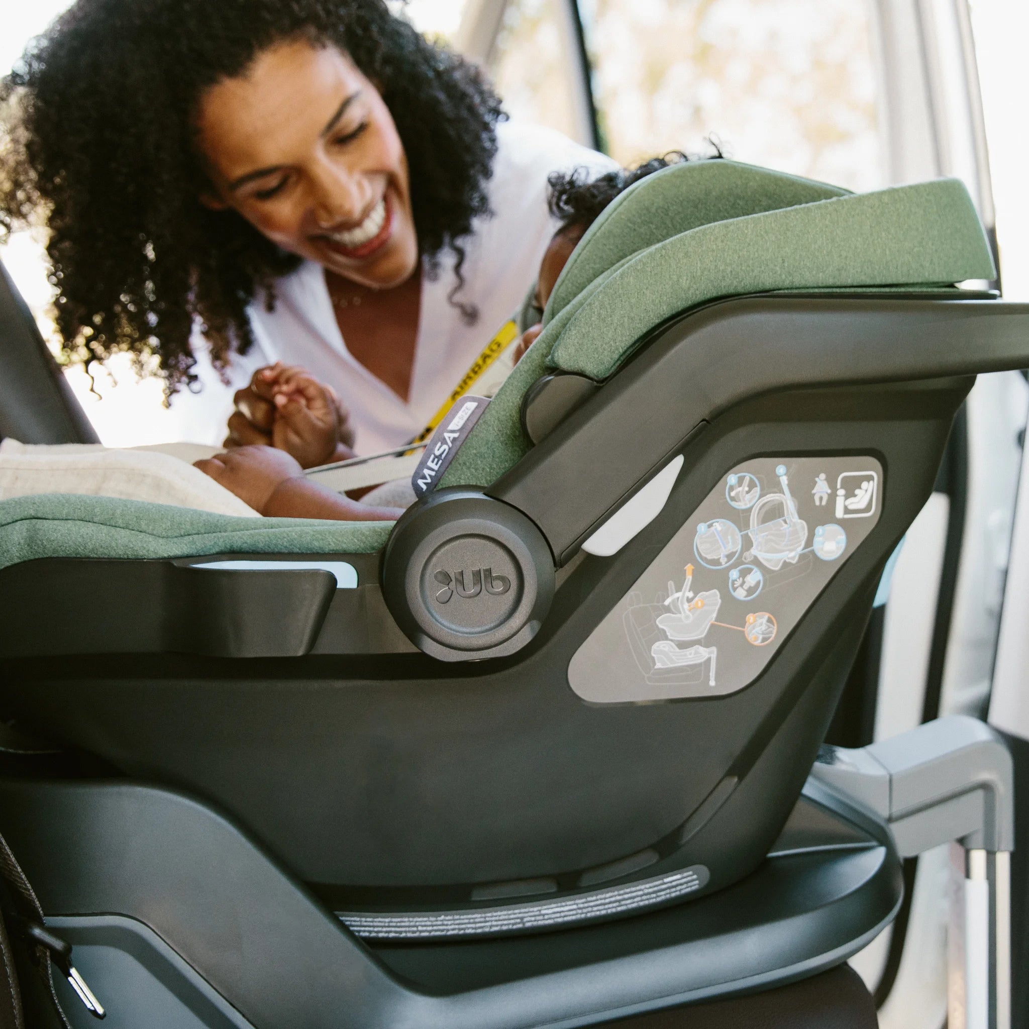 Woman smiling while strapping child into Mesa car seat on isofix base.