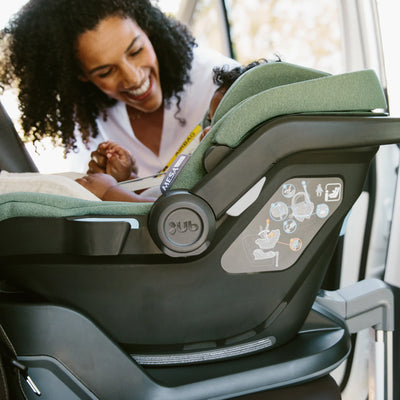 Woman smiling while strapping child into Mesa car seat on isofix base.