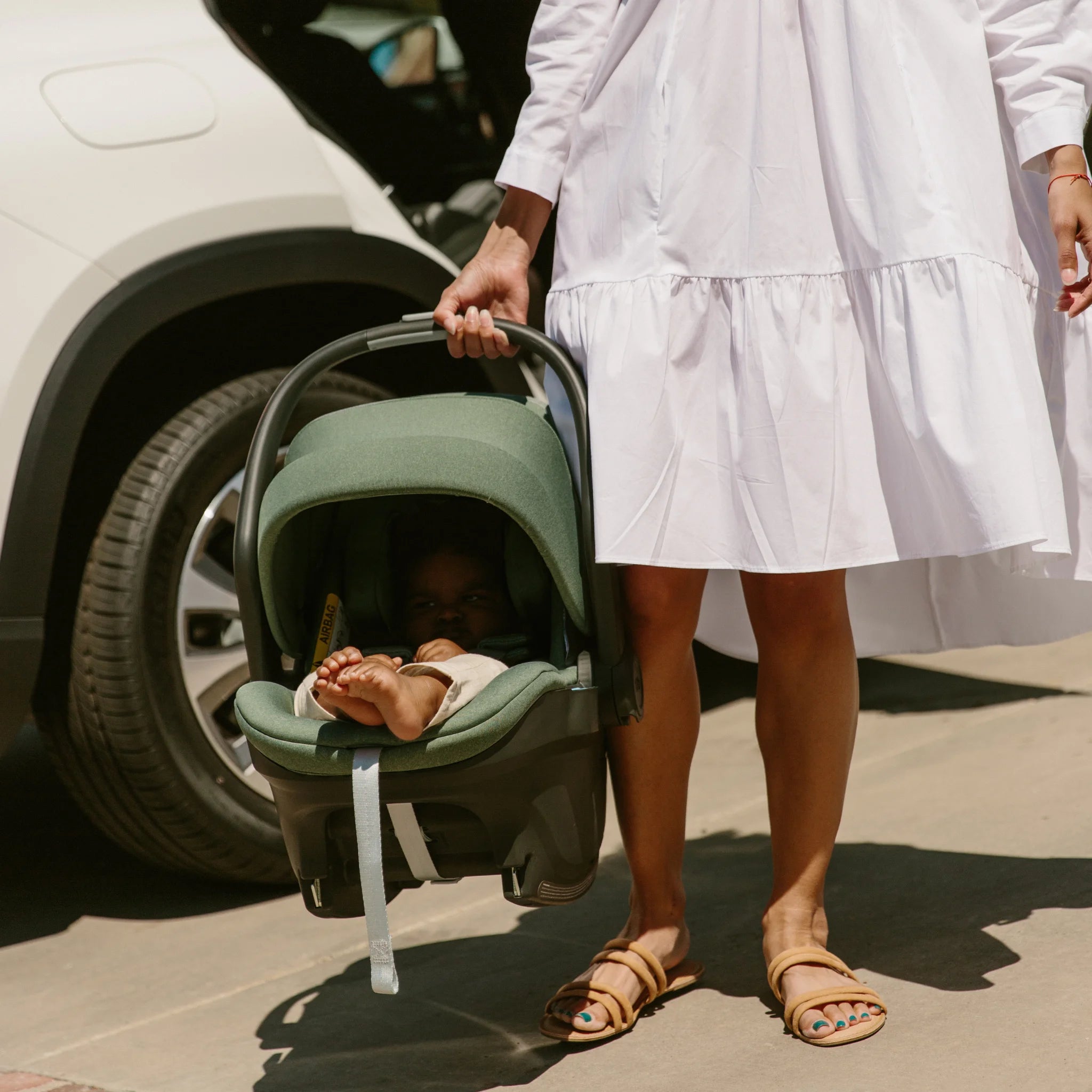 Woman holding the Mesa Gwen infant car seat on a sunny day with canopy extended.