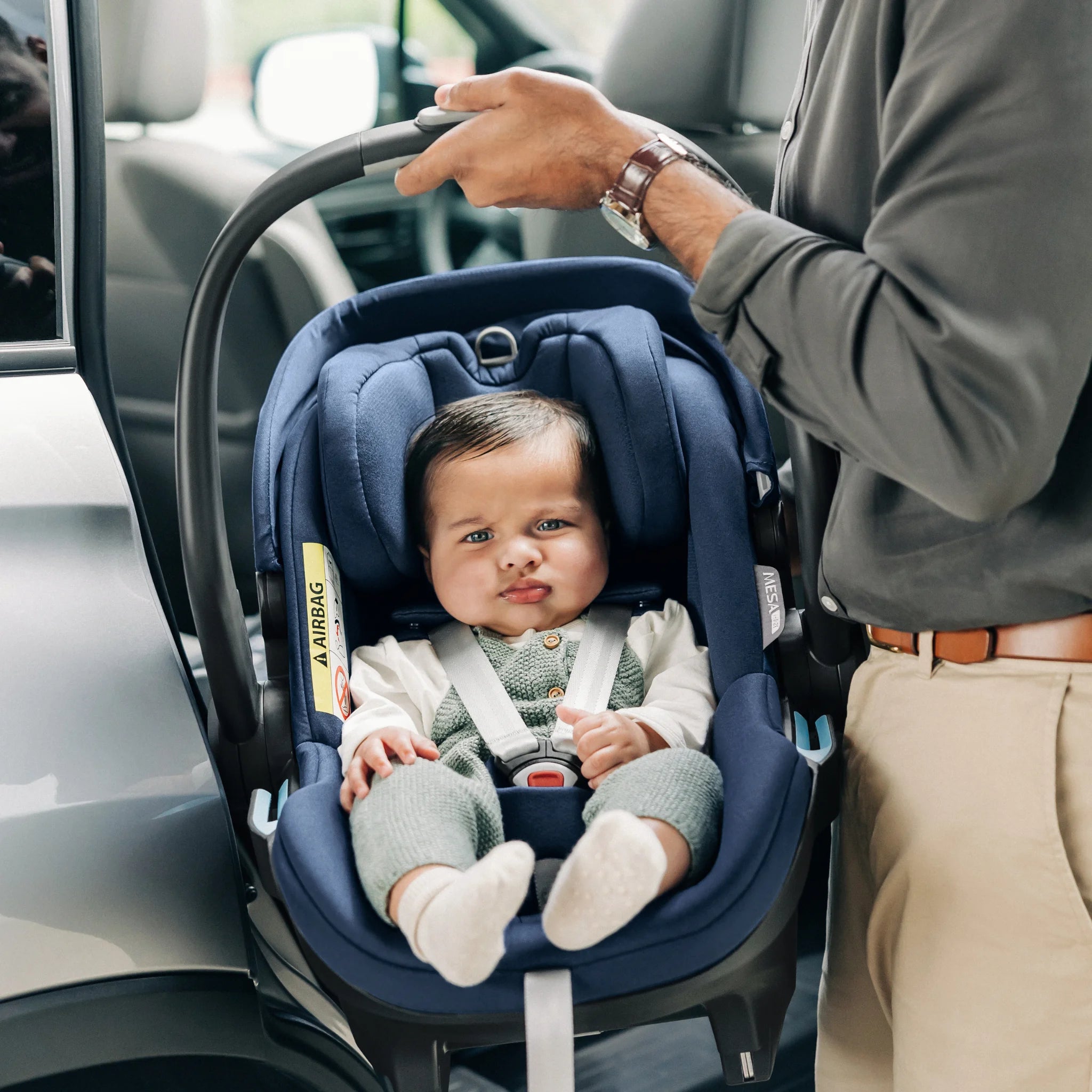 Cute baby sitting in car seat while Dad places it onto the isofix base.