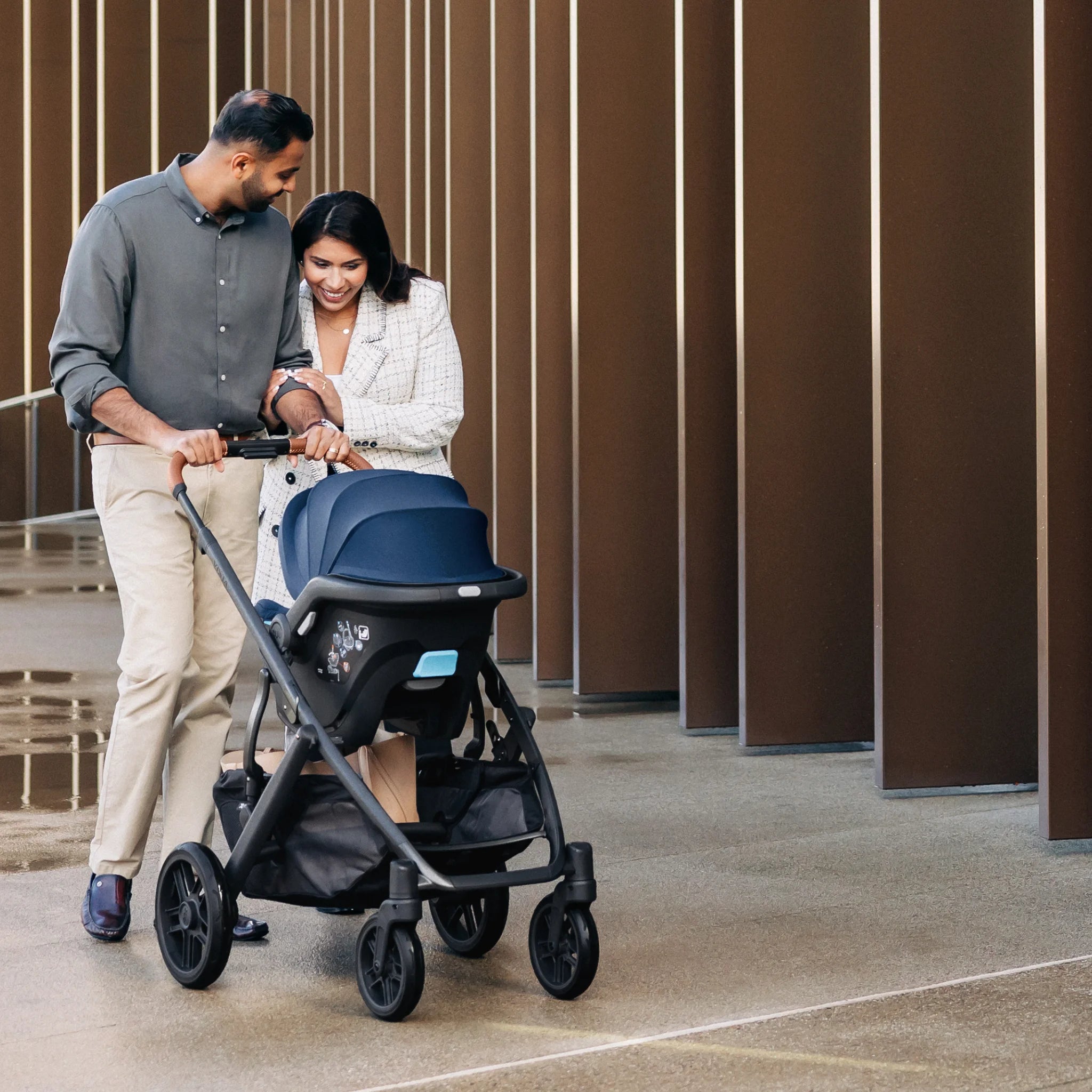 Smiling parents pushing baby in the Vista stroller with Noa car seat attached.