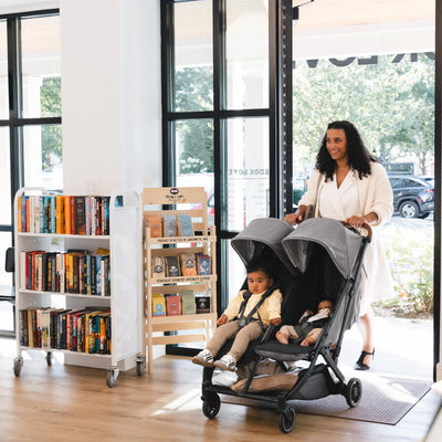 Woman pushing Minu Duo pram into library with toddler and newborn.