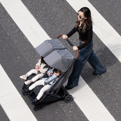 Woman pushing side by side pram with two children on a crosswalk
