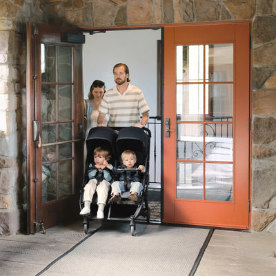 Dad pushing UPPAbaby side-by-side pram easily through narrow doorway.