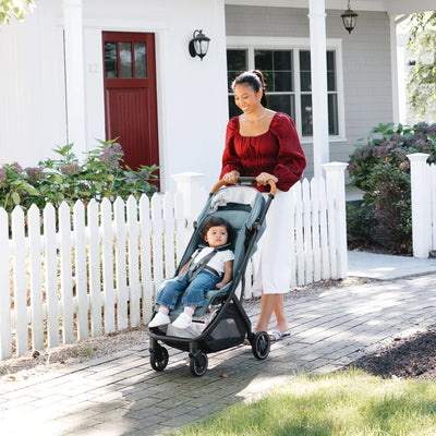 Woman pushing a pram with a child in front of a white house with a red door.