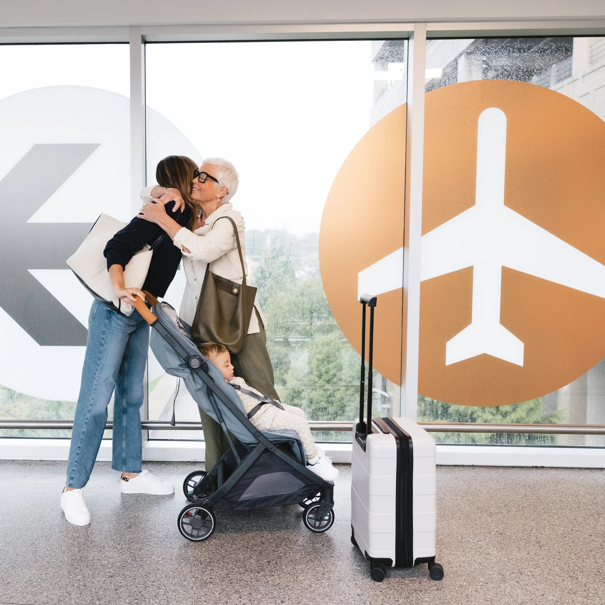 Family with Minu travel stroller and suitcase in an airport terminal.