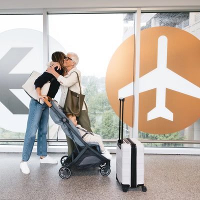 Family with Minu travel stroller and suitcase in an airport terminal.