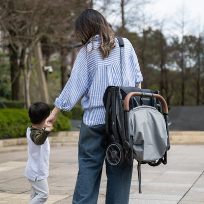 Woman holding a child's hand with the Minu travel stroller over her shoulder with the carry strap.