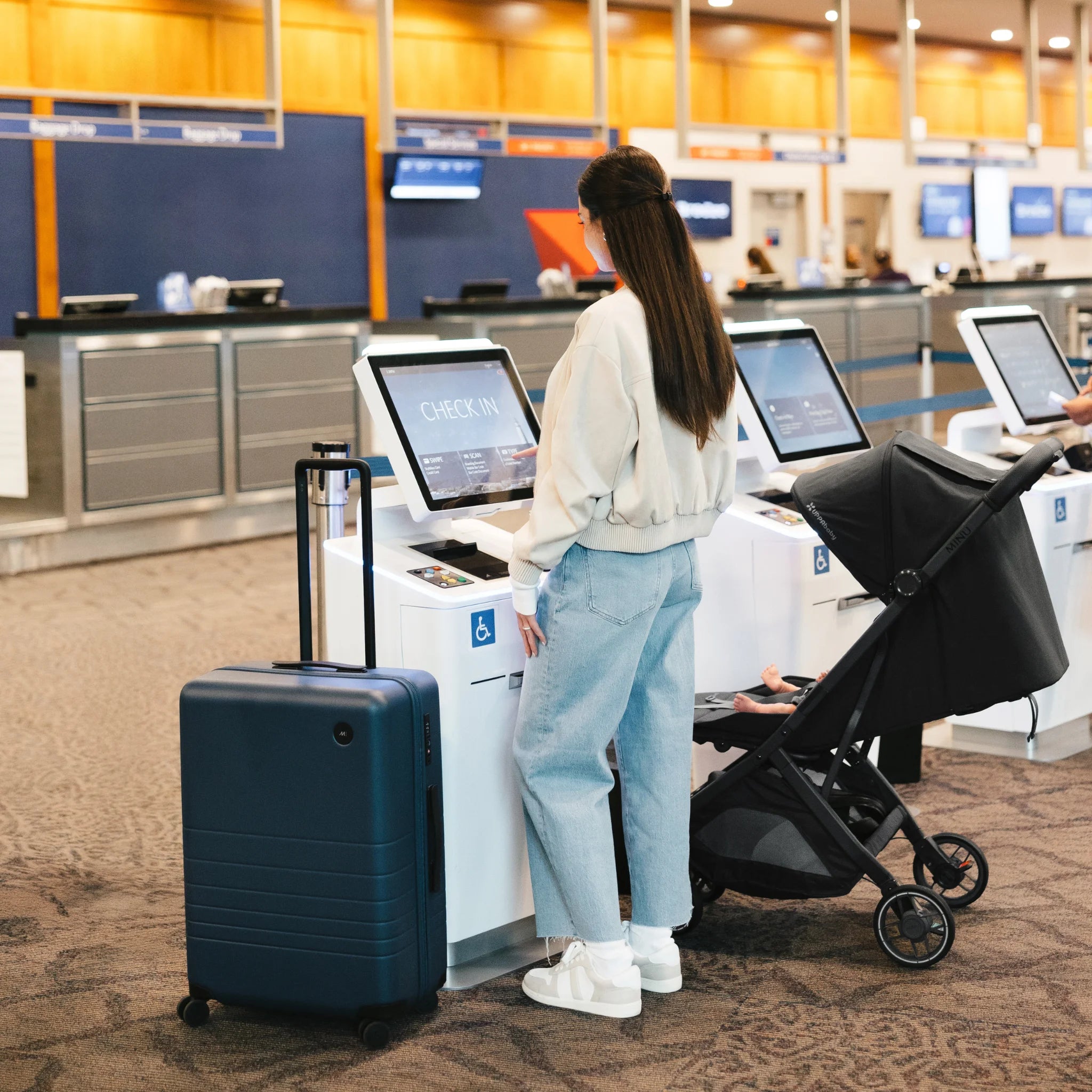 Woman with a suitcase and Minu stroller at an airport check-in counter.