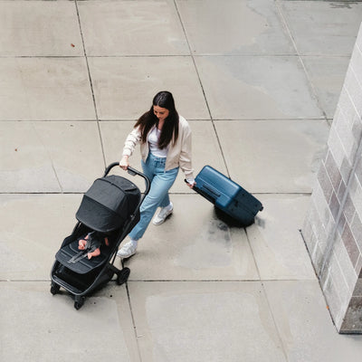 Woman pushing a travel stroller and pulling a suitcase on a sidewalk