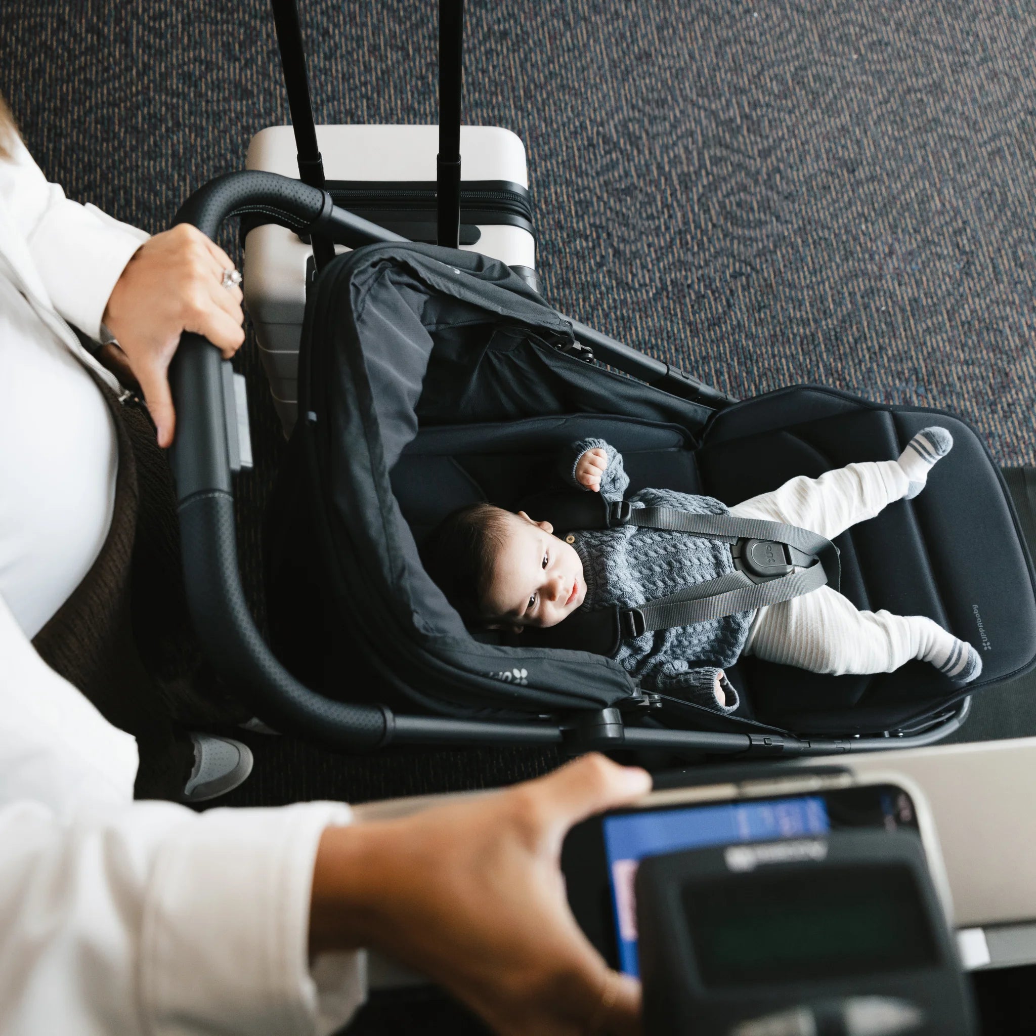 Person holding a baby in a stroller with a phone in hand, scanning their boarding pass.