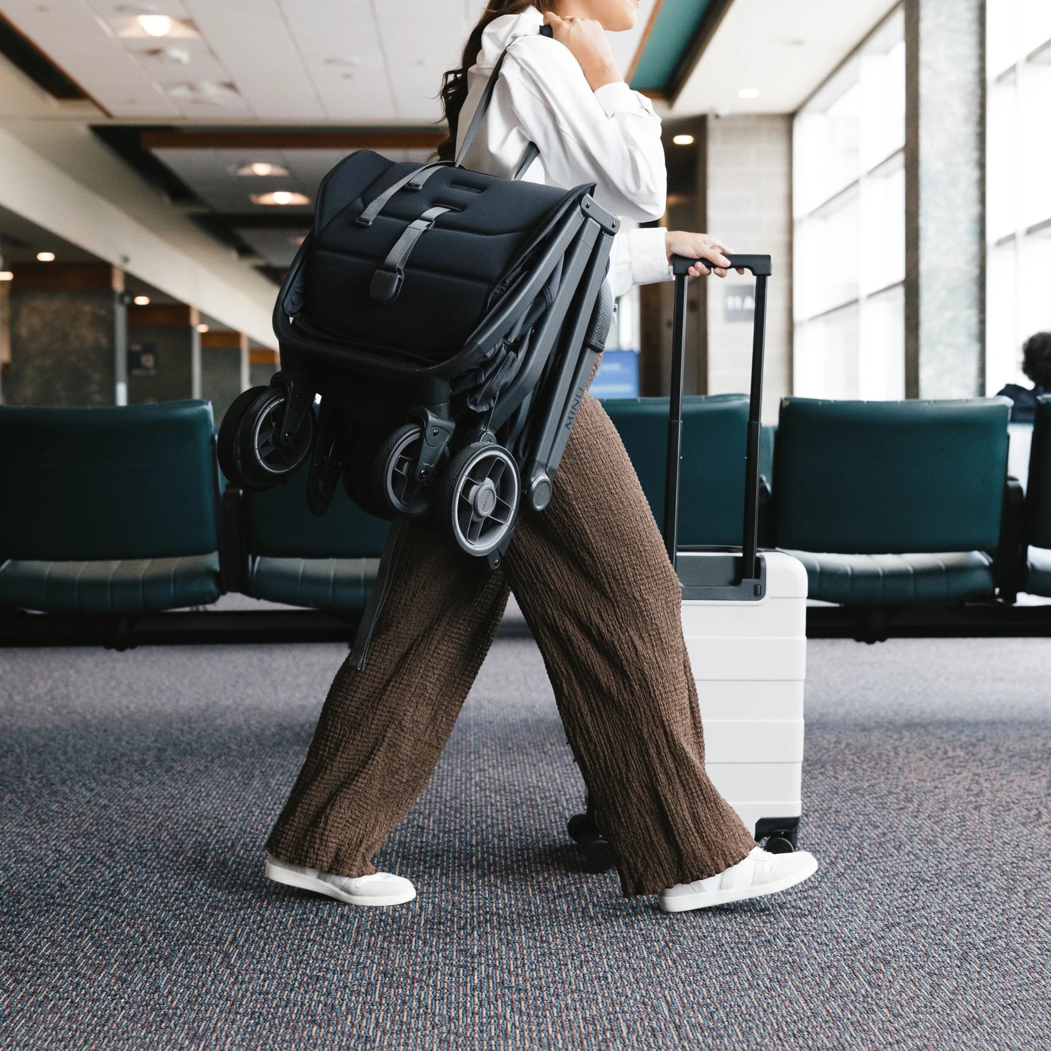 Mum walking through the airport with the Minu travel stroller on their shoulder and wheeling suitcase.