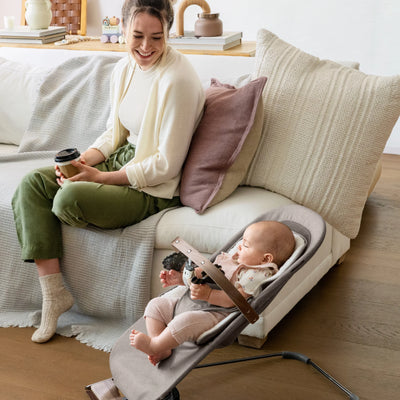 Baby relaxing in the UPPAbaby Mira baby bouncer in Wells while parent sits nearby