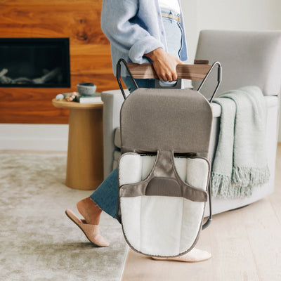 Parent carrying the folded UPPAbaby Mira baby bouncer in Wells
