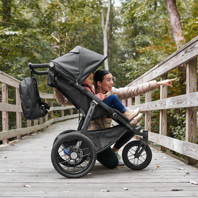 Woman pushing a stroller with a child on a wooden bridge in a forest