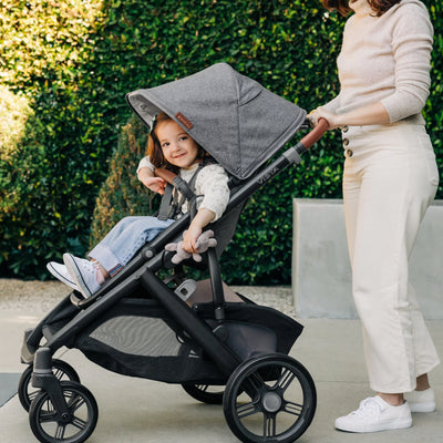 Smiling child being pushed in the Greyson UPPAbaby Vista in front of a green hedge.