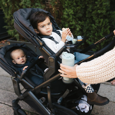Two children in the Vista with parent grabbing coffee cup from the cup holder accessory.