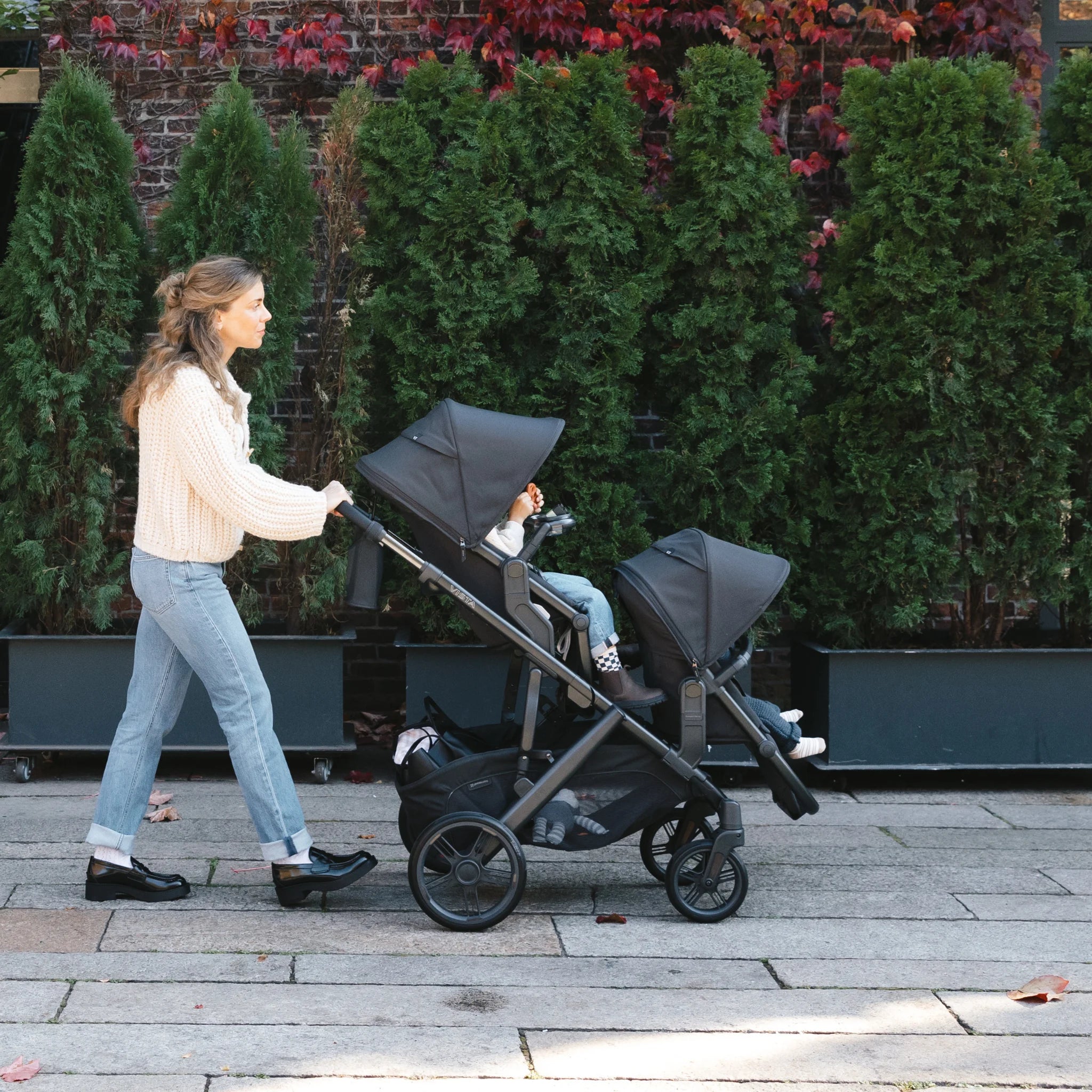 Woman pushing the Vista as a double stroller with two children on a sidewalk.