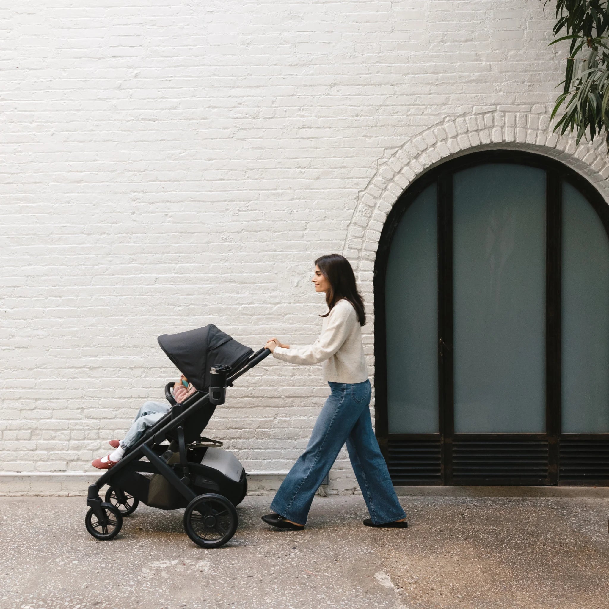 Woman pushing toddler in the Vista in front of a white brick wall.