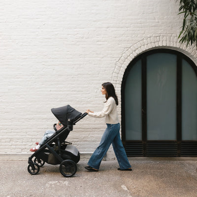 Woman pushing toddler in the Vista in front of a white brick wall.