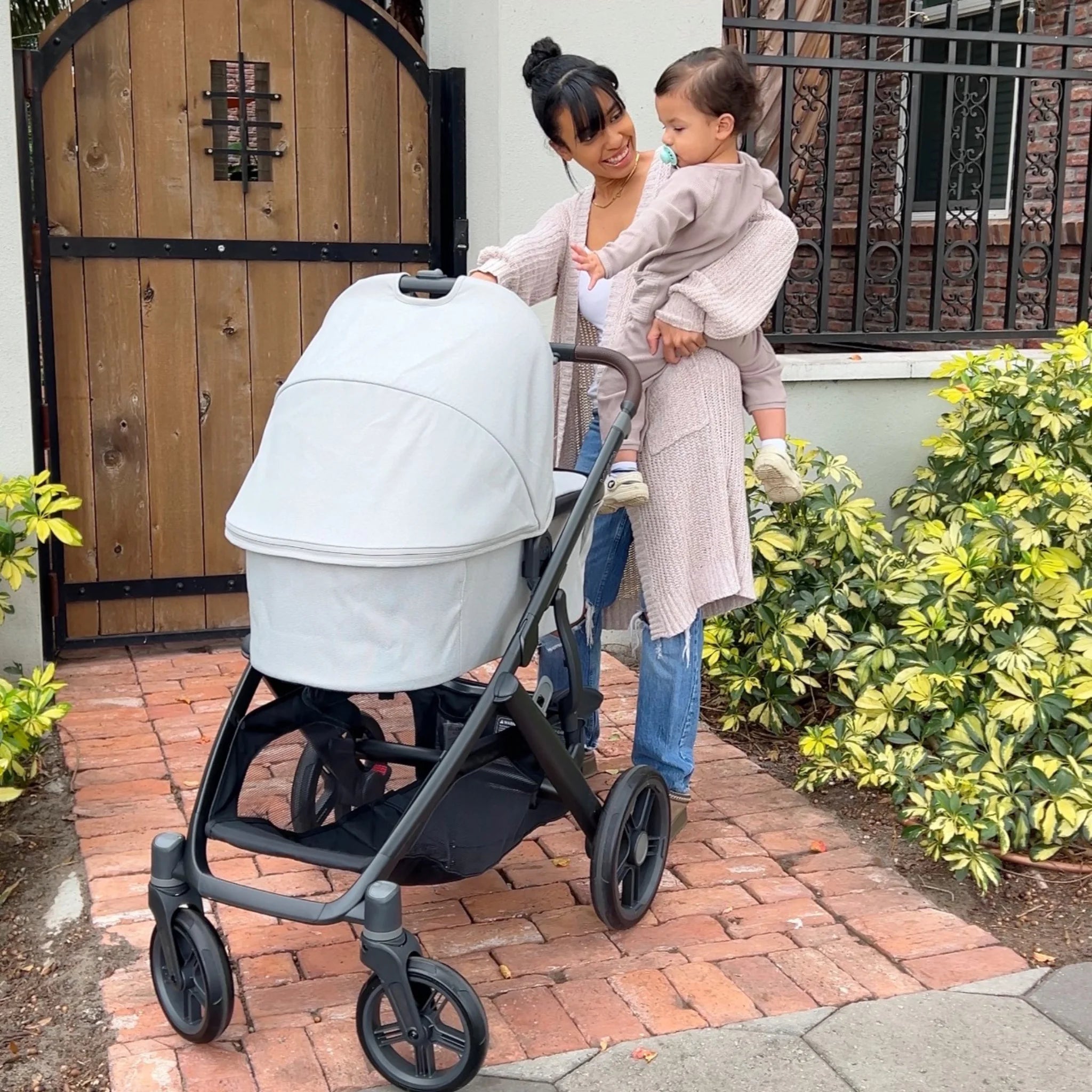 Mum holding baby on hip and chatting to baby in Savannah carrycot.