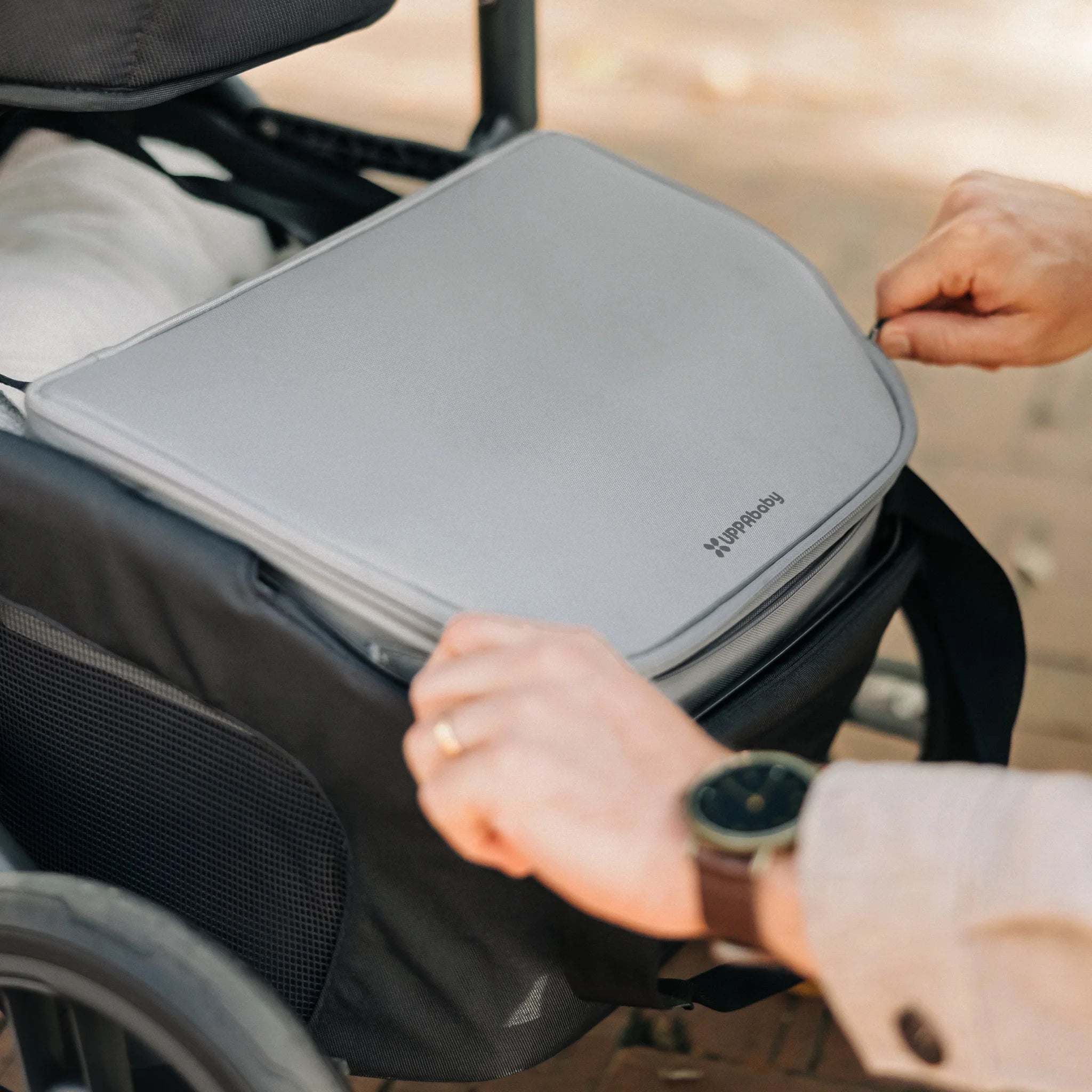 Hands closing the zip on a grey UPPAbaby Bevvy cooler bag in the stroller basket.