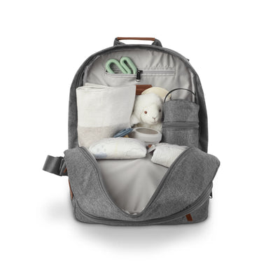 Open Greyson gray changing backpack displayed on a white background, filled with baby essentials including a changing pad, wipes case, bottle holder, toy, and small accessories organized in interior compartments.