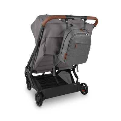 Grey UPPAbaby stroller shown with the matching Greyson changing backpack attached to the handlebar (brown handle accents), on a white background.