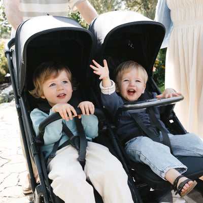 Two children sitting in a UPPAbaby Minu Duo double stroller with the snack tray attached.