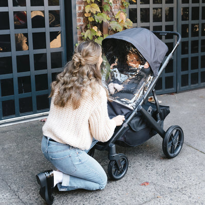Woman adjusting UPPAbaby stroller with UPPAbaby Performance Rain Shield, child inside under clear rain cover