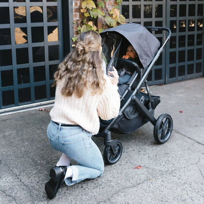 Parent adjusting UPPAbaby stroller with baby inside, using UPPAbaby Performance Rain Shield outdoors