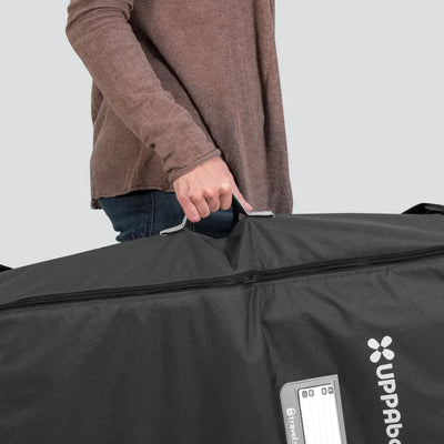 Person carrying UPPAbaby Travel Bag for RumbleSeat or Bassinet by handle, black travel bag with logo