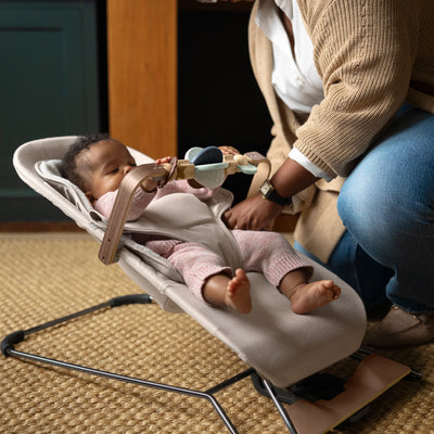 Baby playing with mira wonderwheel toy bar on bouncer seat, indoors. 