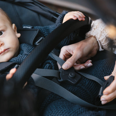 Mum strapping up baby in rumbleseat in the colour jake. 